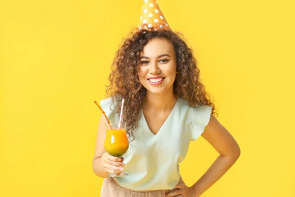 Happy African-American woman in party hat and with cocktail on color background — Stock Photo, Image