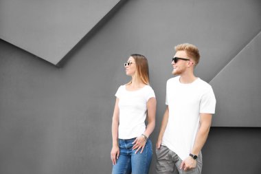 Gri duvara yakın şık tişörtler giymiş erkek ve kadın