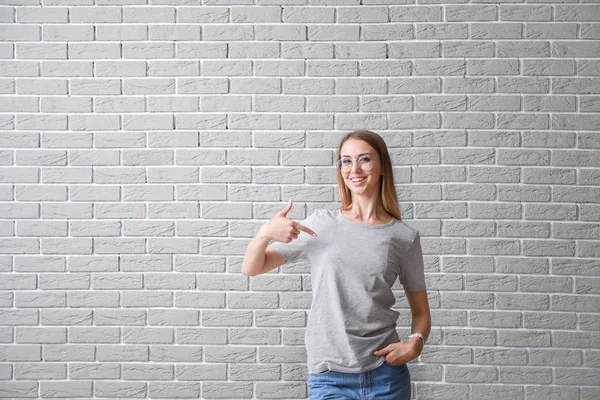 Woman pointing at her t-shirt against brick wall — Stock Photo, Image