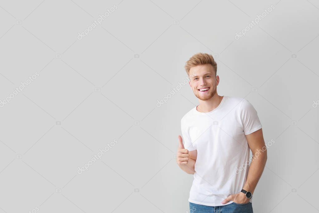 Man in stylish t-shirt showing thumb-up on light background