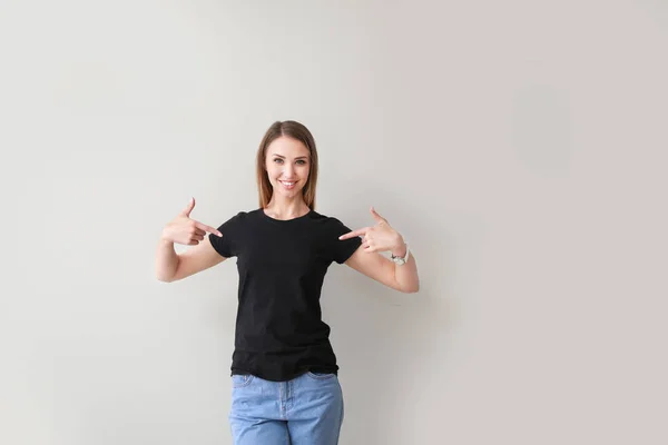 Kvinna som pekar på sin t-shirt mot ljus bakgrund — Stockfoto