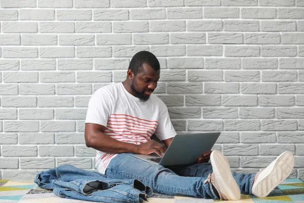 African-American blogger with laptop sitting near brick wall — Stock Photo, Image