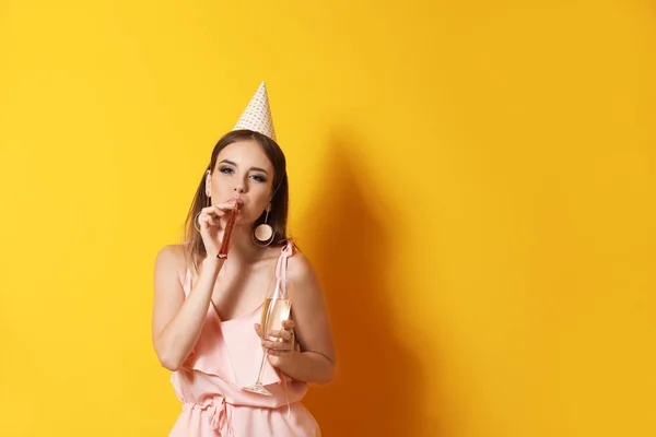 Happy woman with glass of champagne and party whistle on color background — Stock Photo, Image