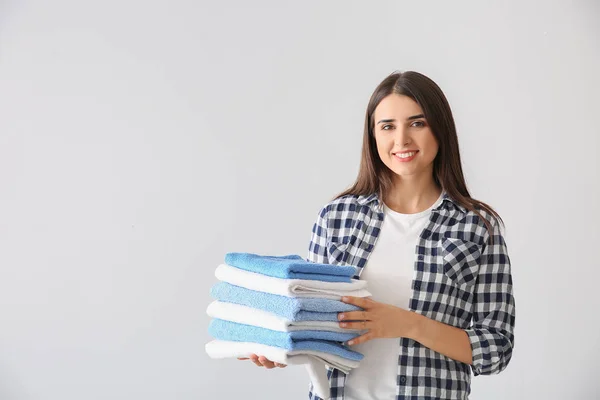 Mooie jonge vrouw met stapel schone handdoeken op lichte achtergrond — Stockfoto