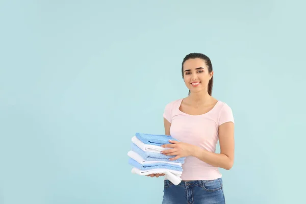 Beautiful young woman with stack of clean towels on color background — Stock Photo, Image
