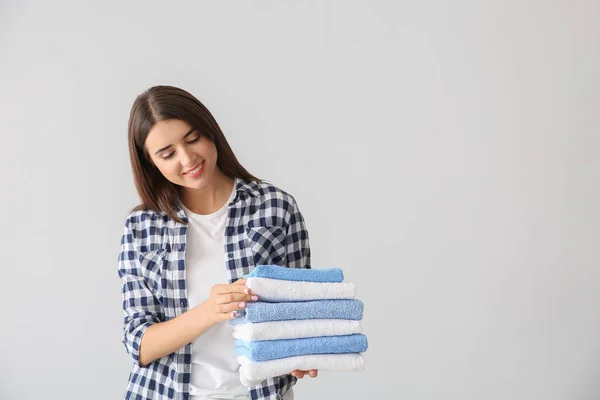 Beautiful young woman with stack of clean towels on light background — Stock Photo, Image