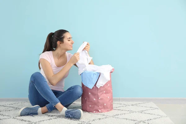 Beautiful young woman with laundry sitting on floor near color wall — Stock Photo, Image