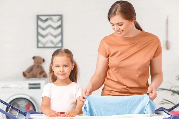 Mother and little daughter hanging laundry on clothes dryer after washing — Stock Photo, Image