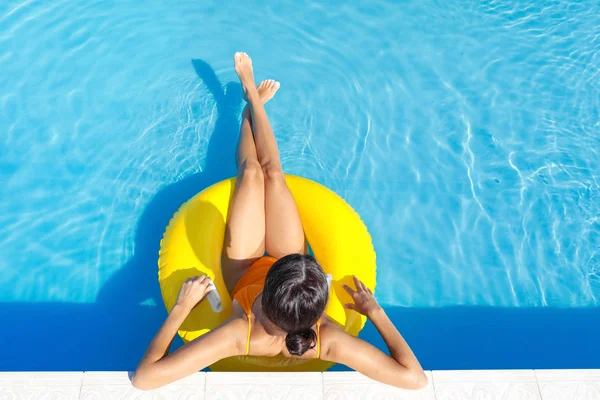 Güzel genç bir kadın yüzme havuzunda şişme yüzükte dinleniyor.