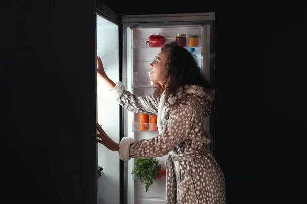 Mujer joven eligiendo comida en el refrigerador por la noche —  Fotos de Stock