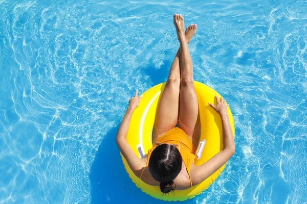 Beautiful young woman relaxing on inflatable ring in swimming pool — Stock Photo, Image
