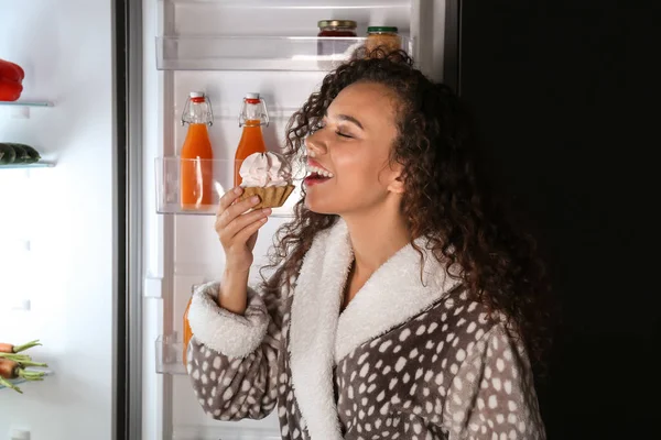 Щаслива жінка їсть смачний торт біля холодильника вночі — стокове фото