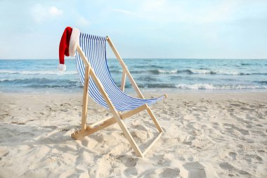Deniz kıyısında Noel Baba şapkalı plaj sandalyesi. Noel tatili
