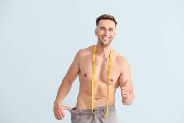 Gevşek pantolon yakışıklı kaslı adam ve renkli arka plan üzerinde bant ölçme ile. Kilo kaybı kavramı