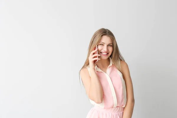 Happy young woman talking by mobile phone on light background — Stock Photo, Image