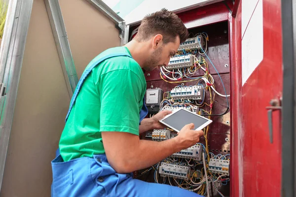 Electrician with tablet computer installing alarm system in distribution board — Stock Photo, Image