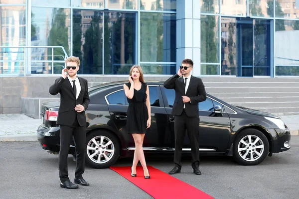 Famous celebrity with bodyguards near car outdoors