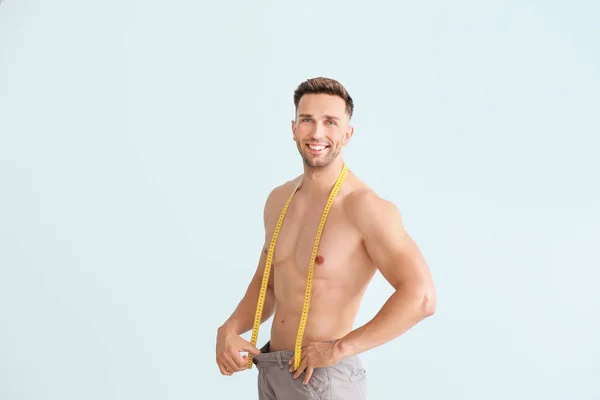 ゆったりしたズボンと色の背景に測定テープでハンサムな筋肉の男。減量の概念 — ストック写真
