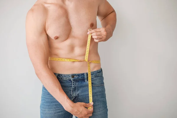 Pohledný svalnatý muž s měřicí páskou na světlého pozadí. Koncepce ztráty váhy — Stock fotografie