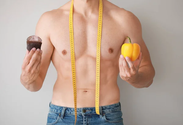 Handsome muscular man with measuring tape, healthy and unhealthy food on light background. Weight loss concept — Stock Photo, Image