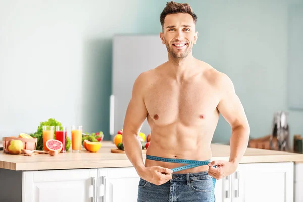 Handsome muscular man with measuring tape in kitchen. Weight loss concept — Stock Photo, Image