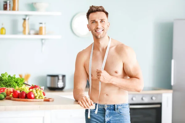 Handsome muscular man with measuring tape in kitchen. Weight loss concept — Stock Photo, Image