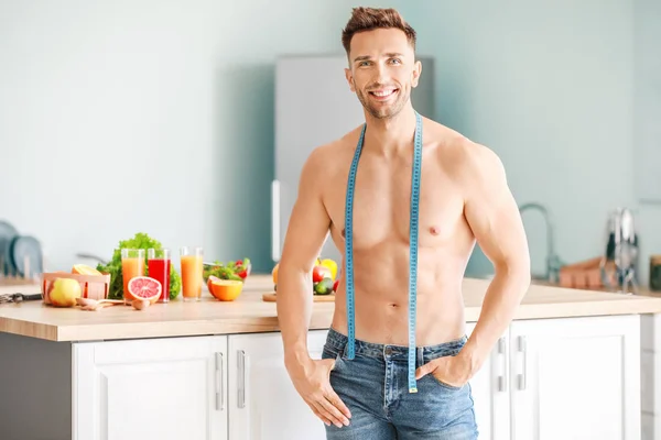 Handsome muscular man with measuring tape in kitchen. Weight loss concept — Stock Photo, Image