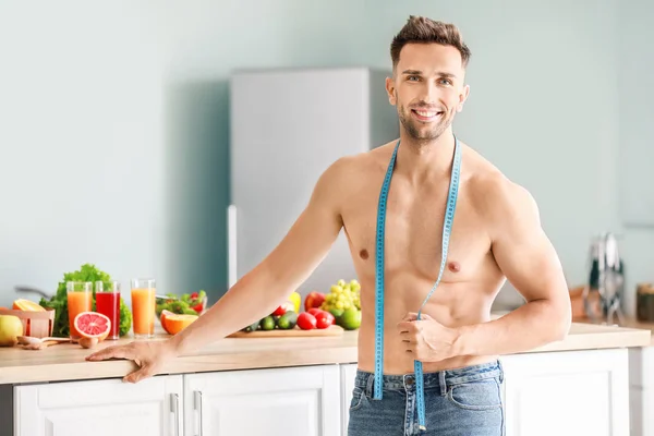 Handsome muscular man with measuring tape in kitchen. Weight loss concept — Stock Photo, Image