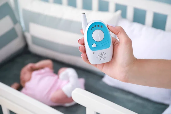 Madre sosteniendo radio niñera cerca de la cama con bebé durmiendo — Foto de Stock