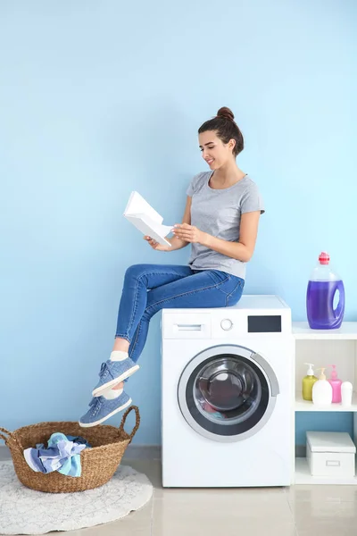 집에서 세탁을하는 동안 책을 읽는 아름다운 젊은 여자 — 스톡 사진