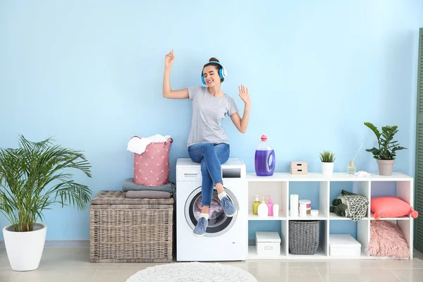 Vacker ung kvinna lyssnar på musik medan du gör tvätt hemma — Stockfoto