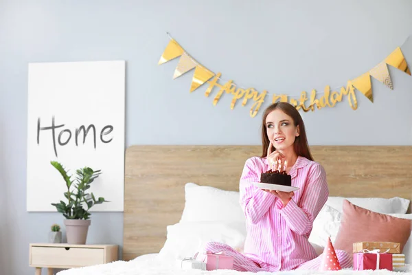 Donna felice con torta di compleanno seduta sul letto a casa — Foto Stock