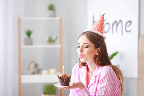 Mujer feliz soplando vela en pastel de cumpleaños en el dormitorio en casa — Foto de Stock
