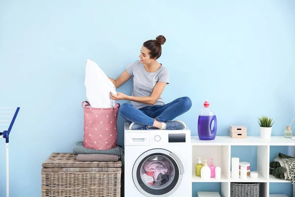 Молодая женщина с чистым бельем сидит дома на стиральной машине — стоковое фото