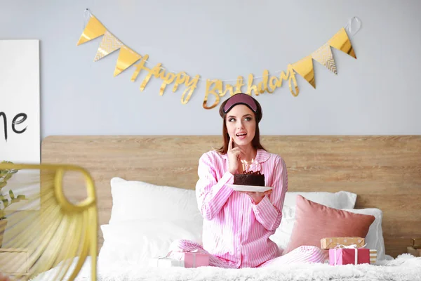Mujer reflexiva con pastel de cumpleaños sentado en la cama en casa — Foto de Stock