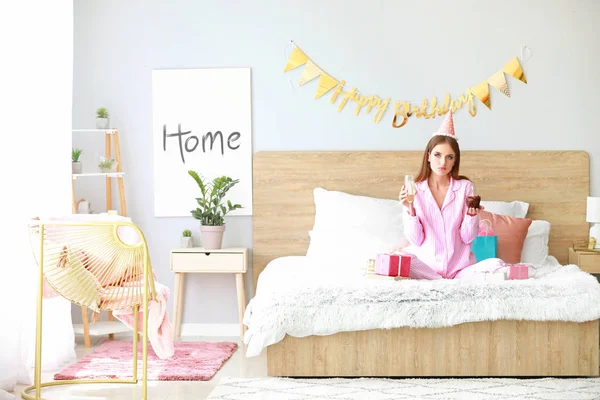 Sad woman with Birthday cake and glass of champagne in bedroom at home — Stock Photo, Image