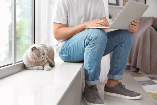 Man with laptop and cute funny cat near window — Stock Photo, Image