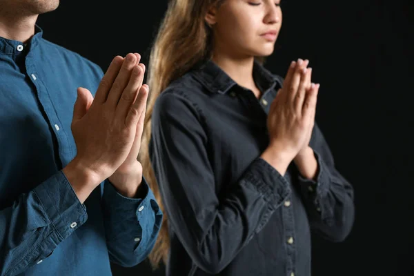 Religious couple praying to God on dark background
