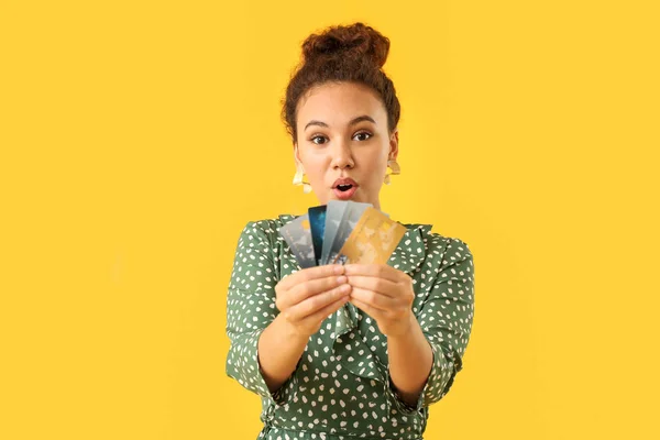 Mulher afro-americana surpresa com cartões de crédito em fundo de cor — Fotografia de Stock