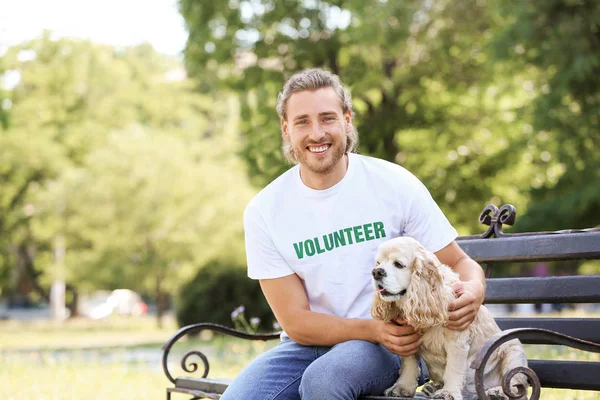 Male volunteer with cute dog sitting on bench outdoors — Stock Photo, Image