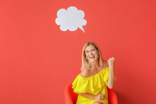 Happy woman sitting in armchair near speech bubble on color background — Stock Photo, Image