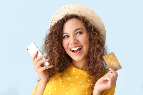 Happy African-American woman with credit card and mobile phone on light color background — Stock Photo, Image