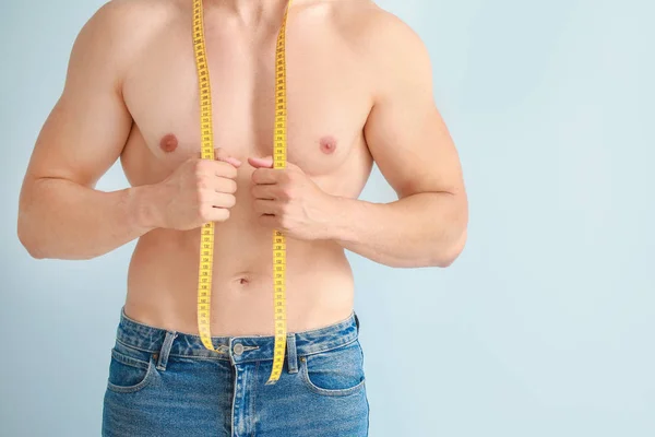 Handsome muscular man with measuring tape on color background. Weight loss concept — Stock Photo, Image