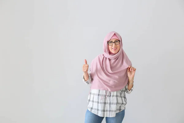 Portrait of Muslim middle-aged woman showing thumb-up gesture on light background — Stock Photo, Image