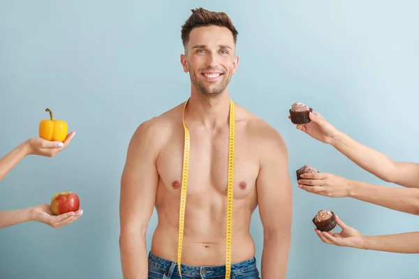 Handsome muscular man with measuring tape and hands suggesting him different food against color background. Weight loss concept — Stock Photo, Image