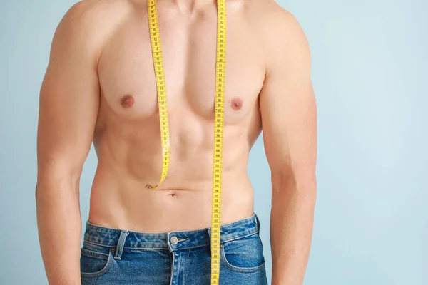 Pohledný svalnatý muž s měřicí páskou na barevném pozadí. Koncepce ztráty váhy — Stock fotografie