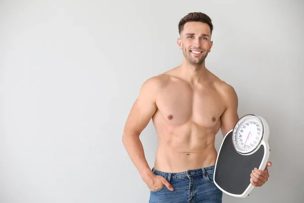 Handsome muscular man with scales on light background. Weight loss concept — Stock Photo, Image