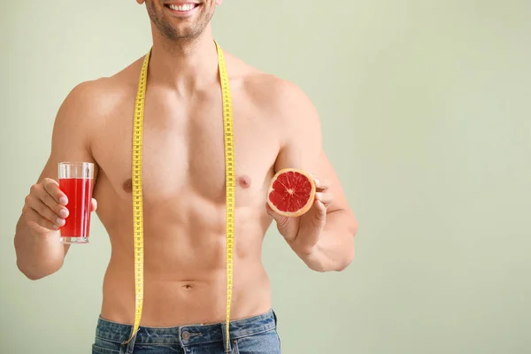 Stilig muskulös man med måttband, grapefrukt och saft på färg bakgrund. Viktminsknings koncept — Stockfoto