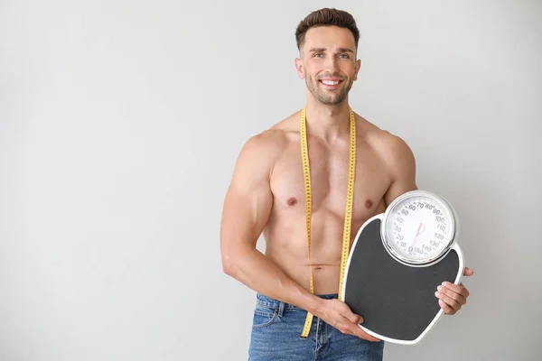 Handsome muscular man with measuring tape and scales on light background. Weight loss concept — Stock Photo, Image