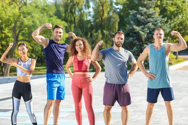 Groep jonge sportieve mensen die spieren buitenshuis tonen — Stockfoto